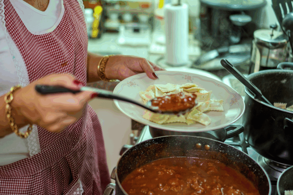 Mani di una donna che versa sugo sui ravioli fatti in casa, simbolo di cibo e conforto come gesto d’amore quotidiano.