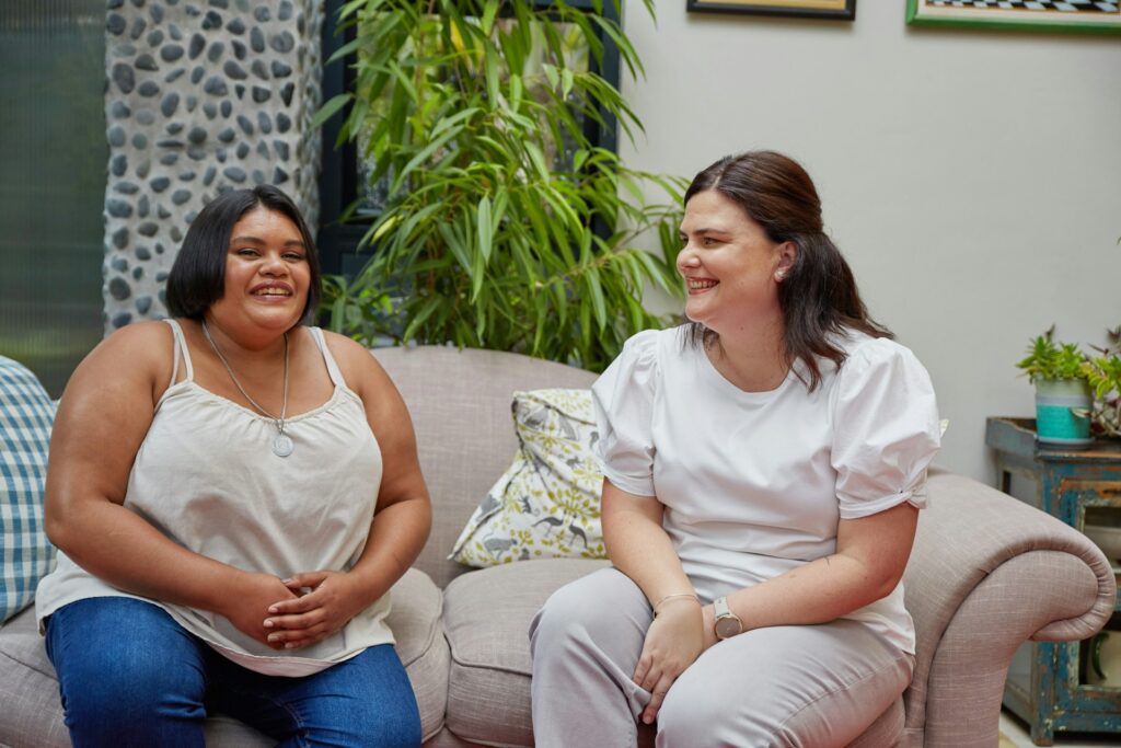 Solidarietà femminile rappresentata da due donne che conversano e sorridono, creando uno spazio di ascolto e sostegno reciproco.