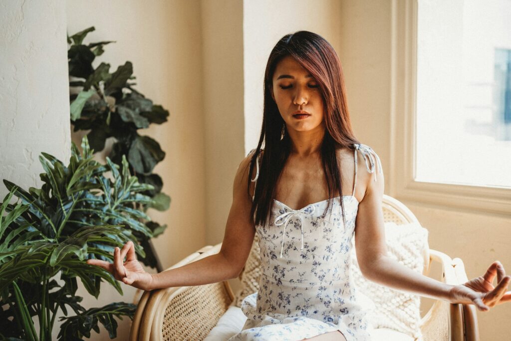 Donna seduta in meditazione vicino a una finestra, simbolo di meditazione, respiro e conforto interiore come pratica di ascolto di sé.