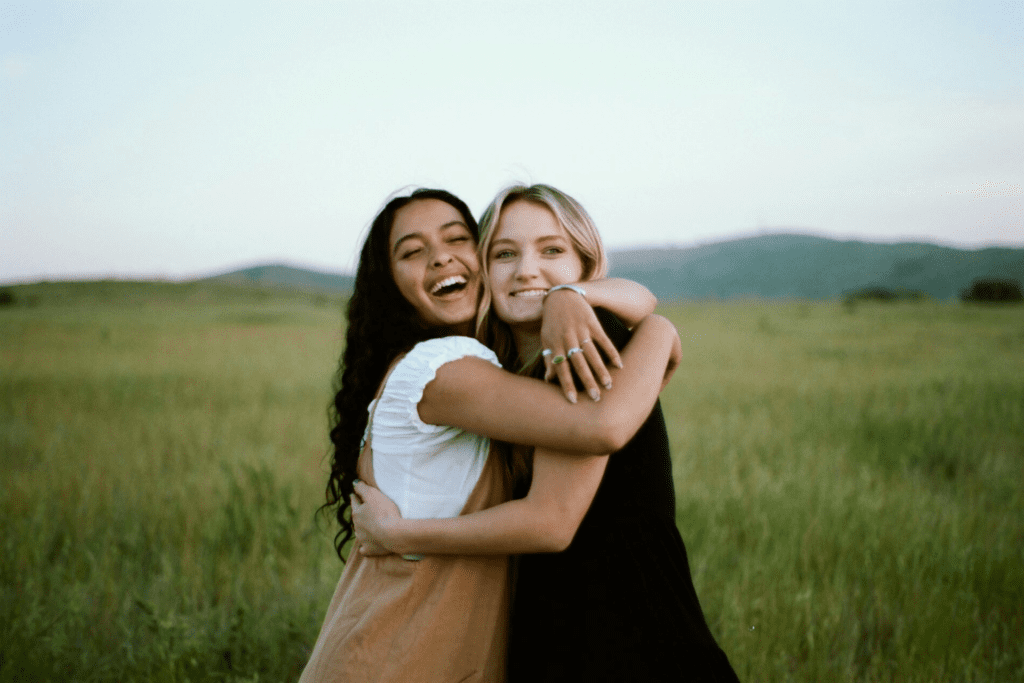 Amicizia femminile: due giovani donne sorridenti si abbracciano in un campo verde, simbolo di sostegno reciproco, fiducia e legame tra amiche.