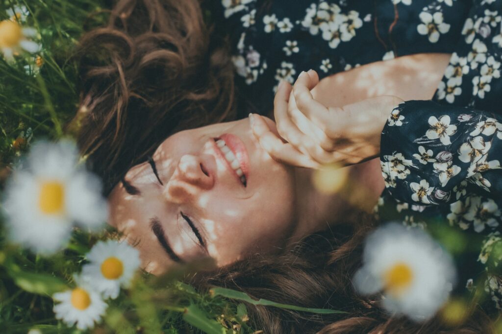 Donna distesa tra i fiori con gli occhi chiusi in un momento di calma, simbolo di come costruire un rifugio interiore e ritrovare conforto emotivo.