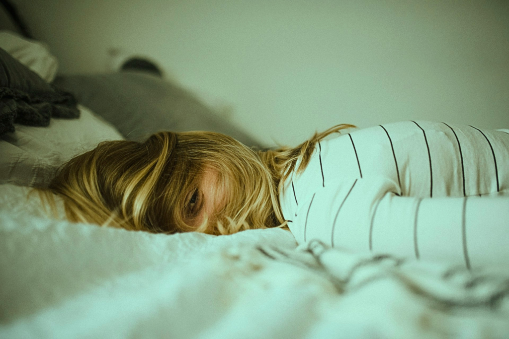 Donna sdraiata sul letto con espressione affaticata, immagine che rappresenta la stanchezza emotiva nelle donne e il bisogno di conforto emotivo, riposo e cura di sé.